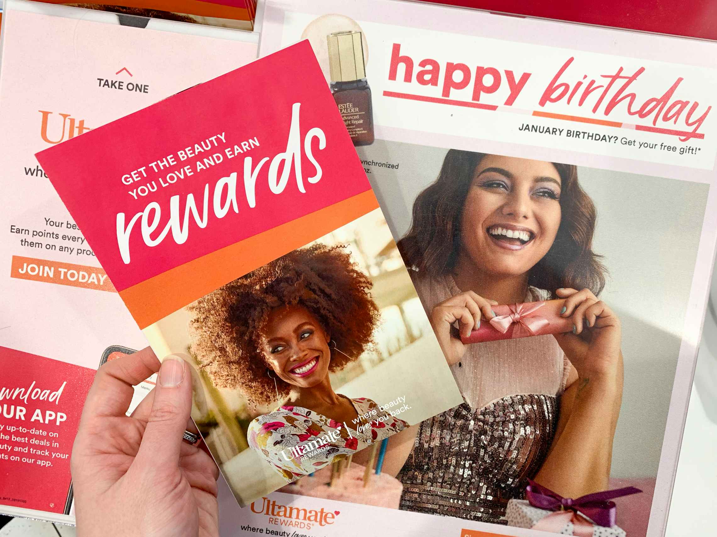 An Ulta rewards brochure held in front of a sign for a "Happy Birthday" free gift.