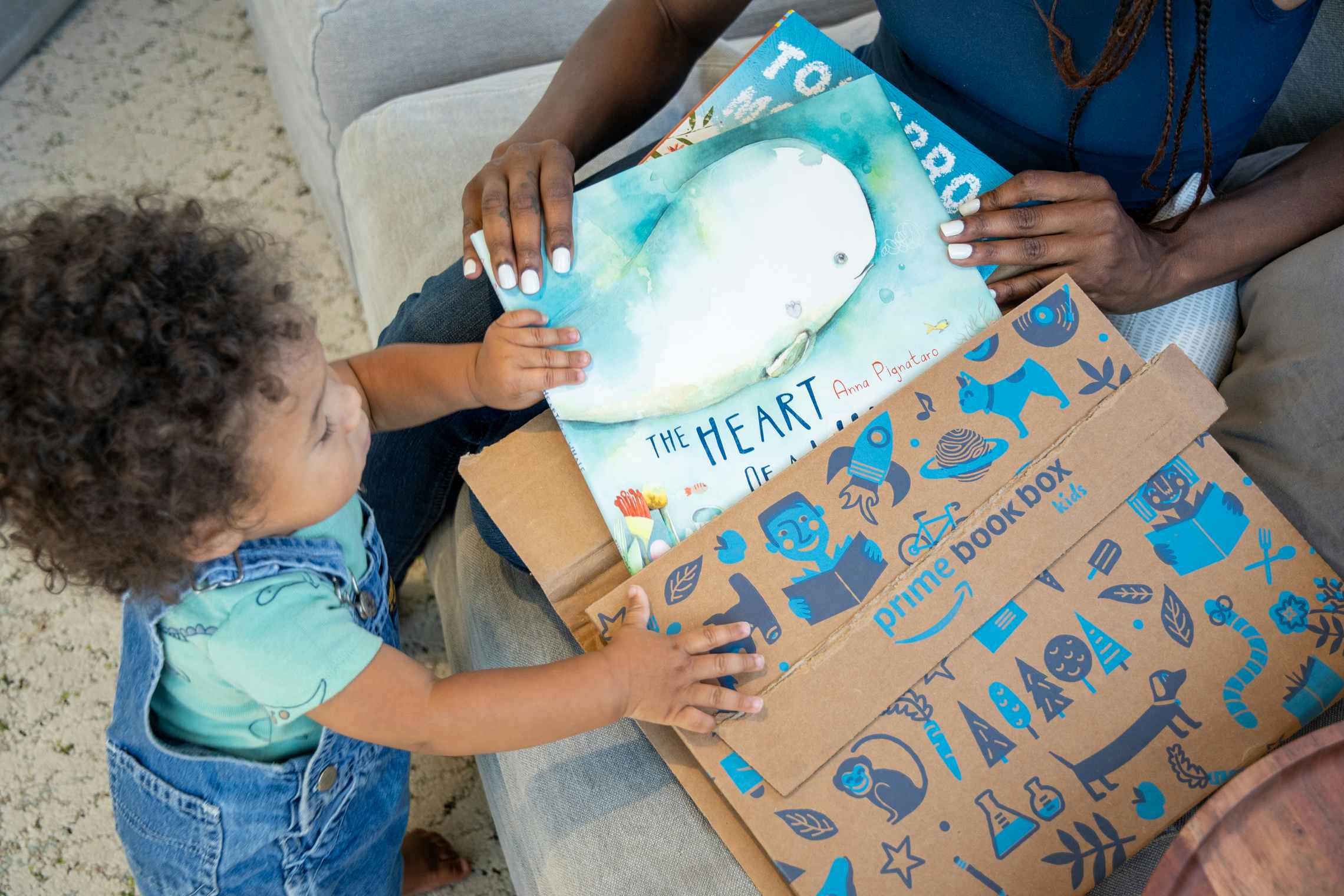 A woman pulling two kids books out of an Amazon Prime Book Box with her child helping.