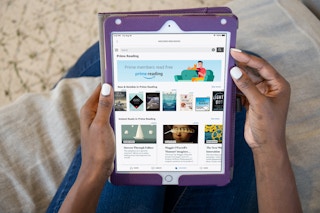 A woman sitting on a couch, holding an iPad which is displaying the Amazon website's page for Prime Reading.