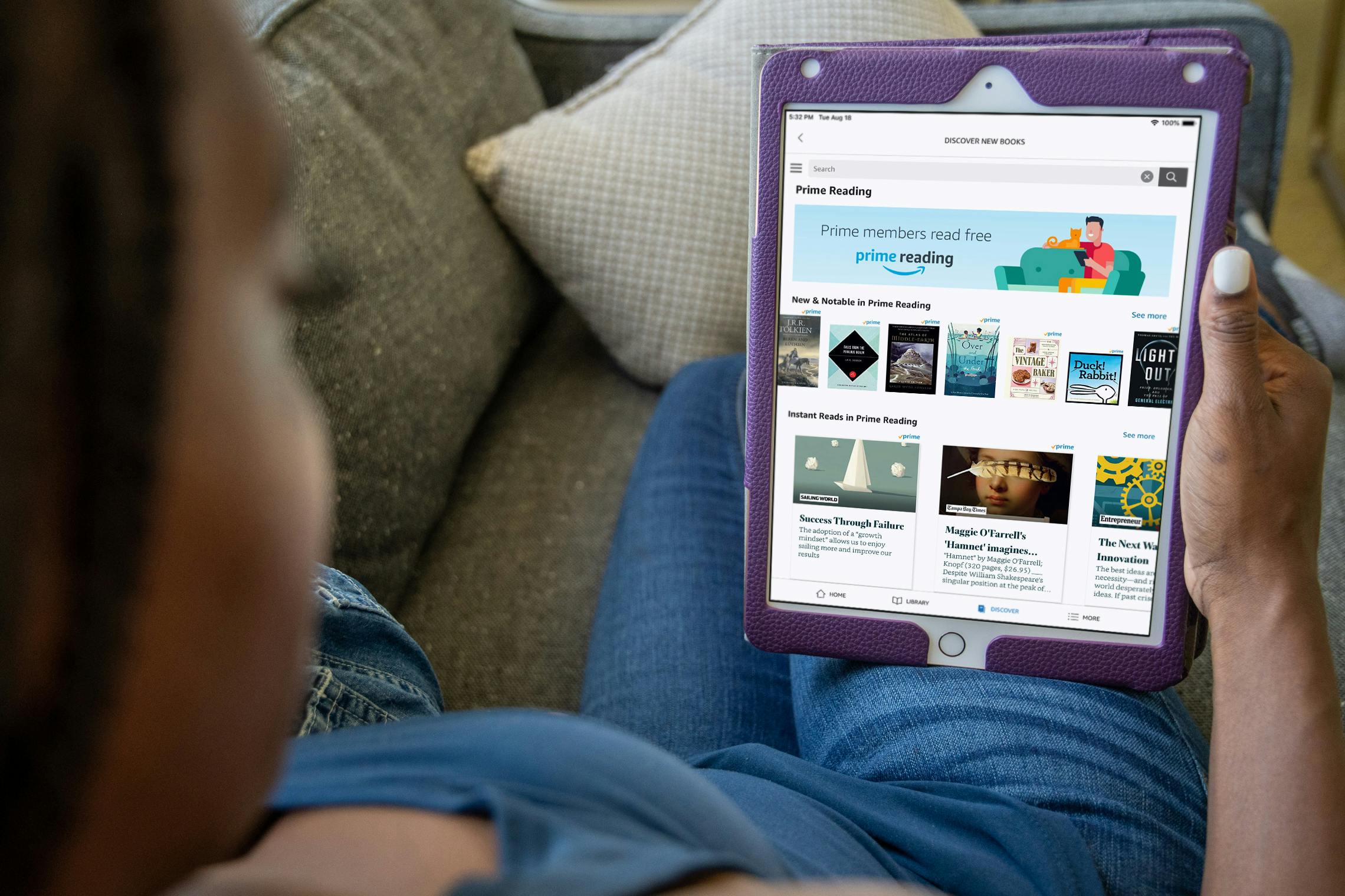 A woman sitting on a couch, looking down at an iPad which is displaying the Amazon website's page for Prime Reading.
