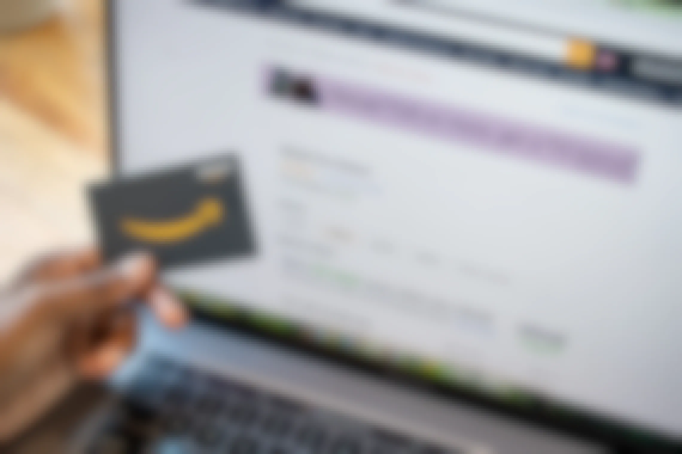 A woman holding an Amazon gift card in front of a computer screen with the Amazon gift card reload page up on it.