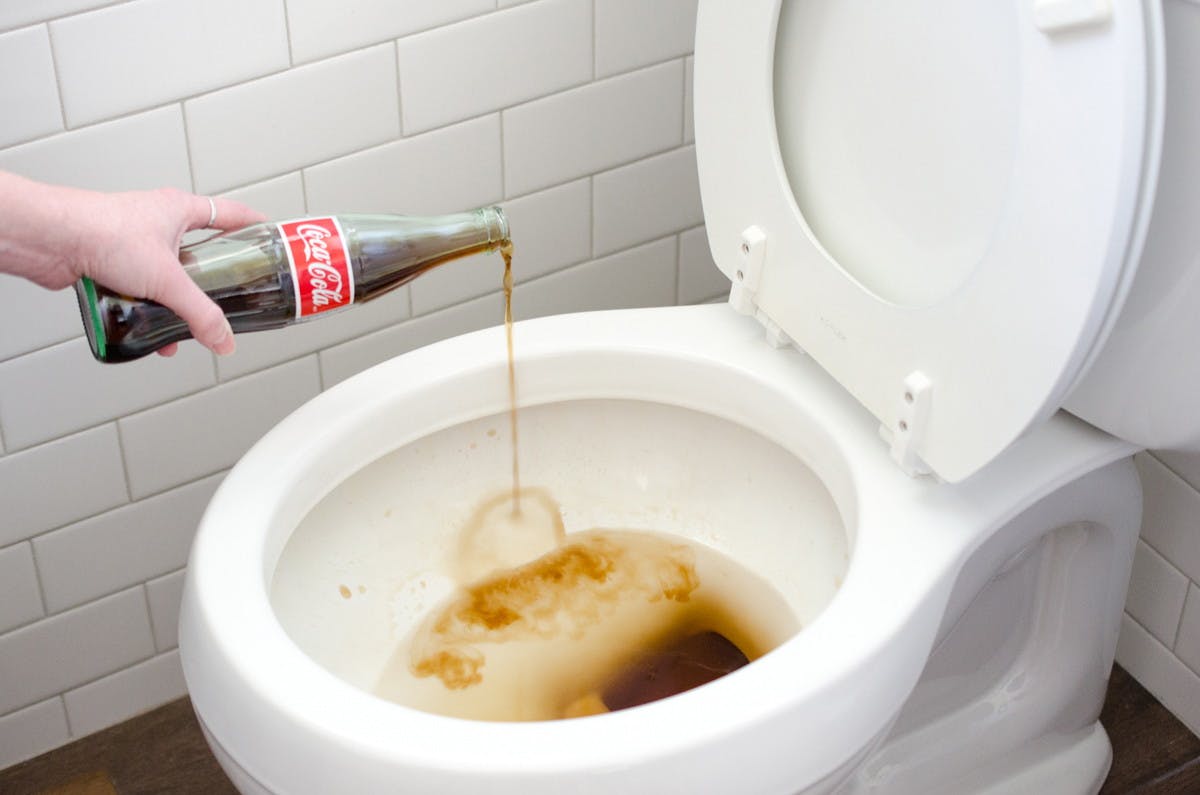 Someone pouring a bottle of Coca Cola into a toilet