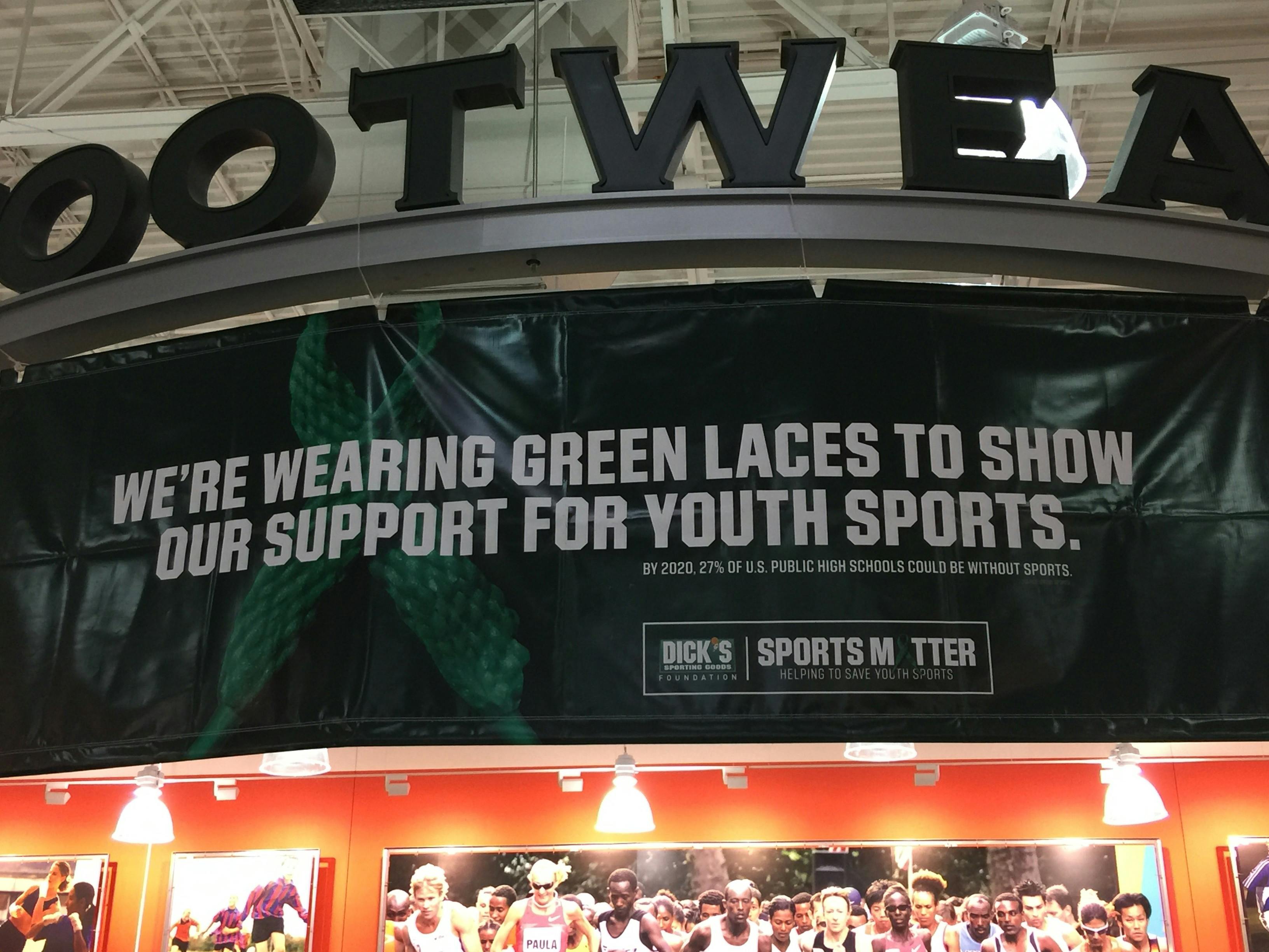 A banner inside a Dick's Sporting Goods store that reads, "We're wearing green laces to show our support for youth sports.
