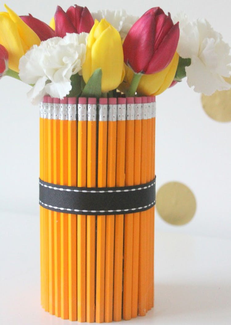 Pencils standing up wrapped with a ribbon around a vase holding a bouquet of flowers.