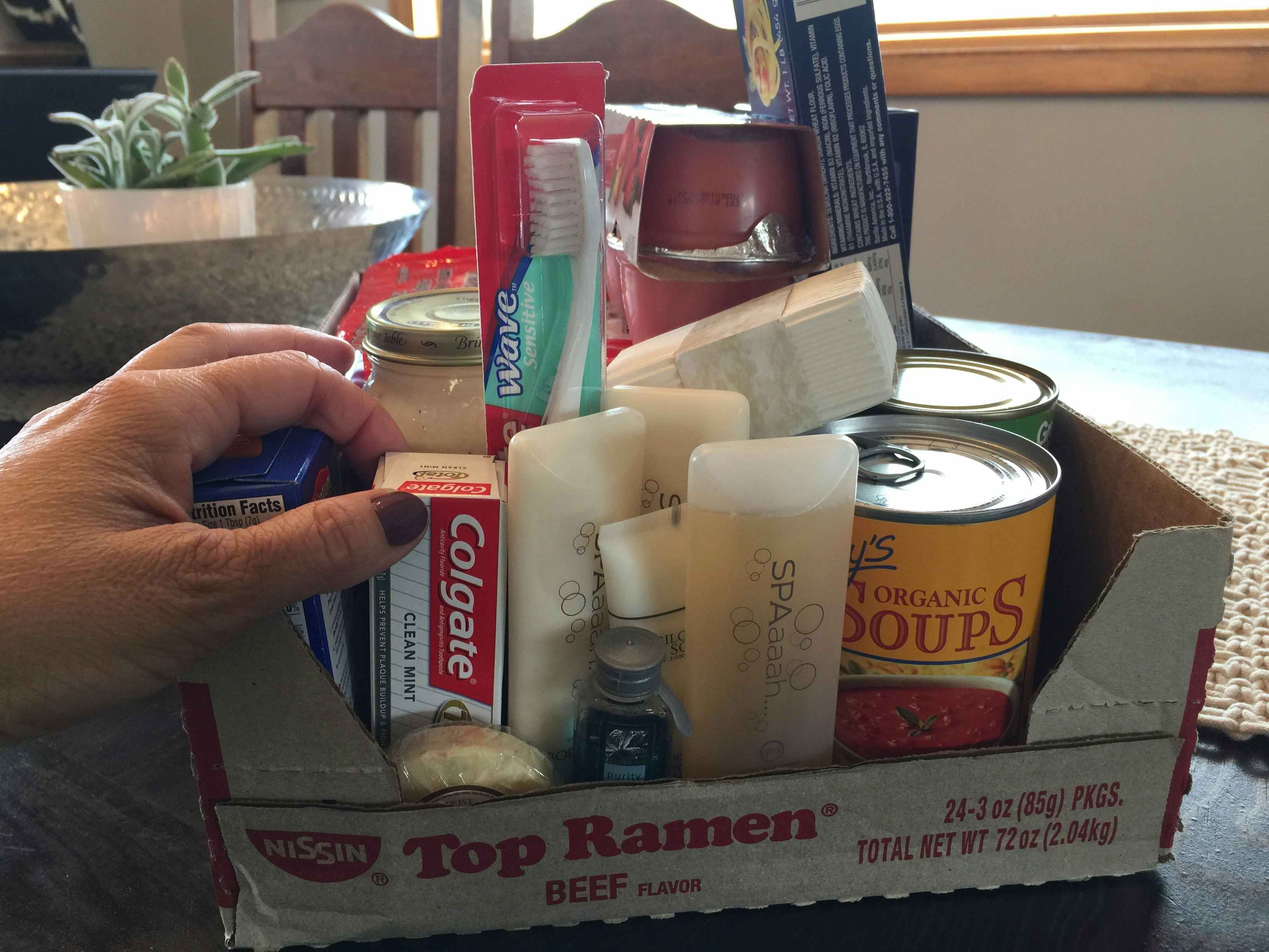 A person holding a tube of toothpaste in a box with other toiletries.