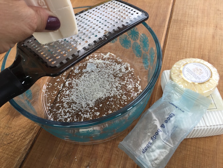 A person grating a bar of soap into a bowl.
