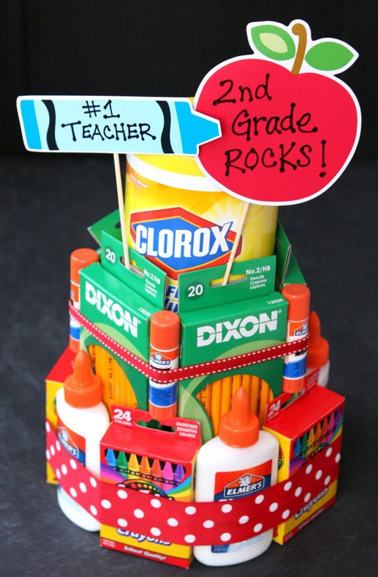 The shape of a cake made out of stacking crayons,pencils, glue bottles and clorox wipes with two flags sticking out the top saying number one teacher and second grade rocks.