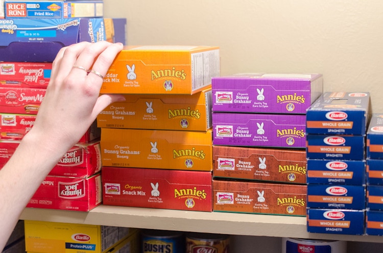 Someone laying boxed foods on their side in on a shelf so more can fit.
