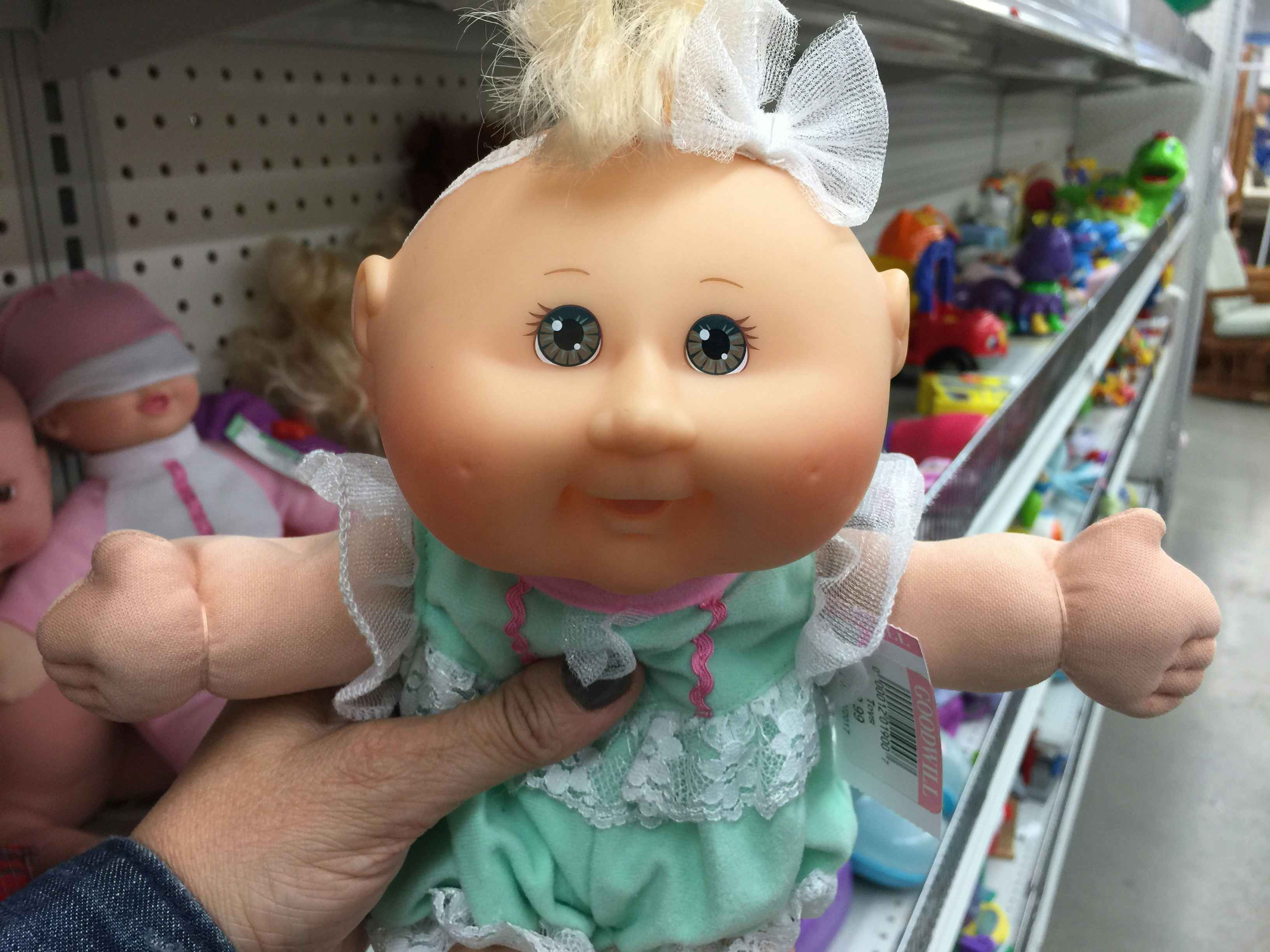 Someone holding up a Cabbage Patch doll in a thrift store