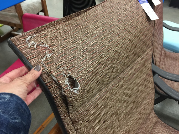 A person looking at a damaged chair in a thrift store