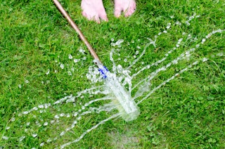 A water bottle with holes drilled into it that has been attached to a hose to make a DIY sprinkler.