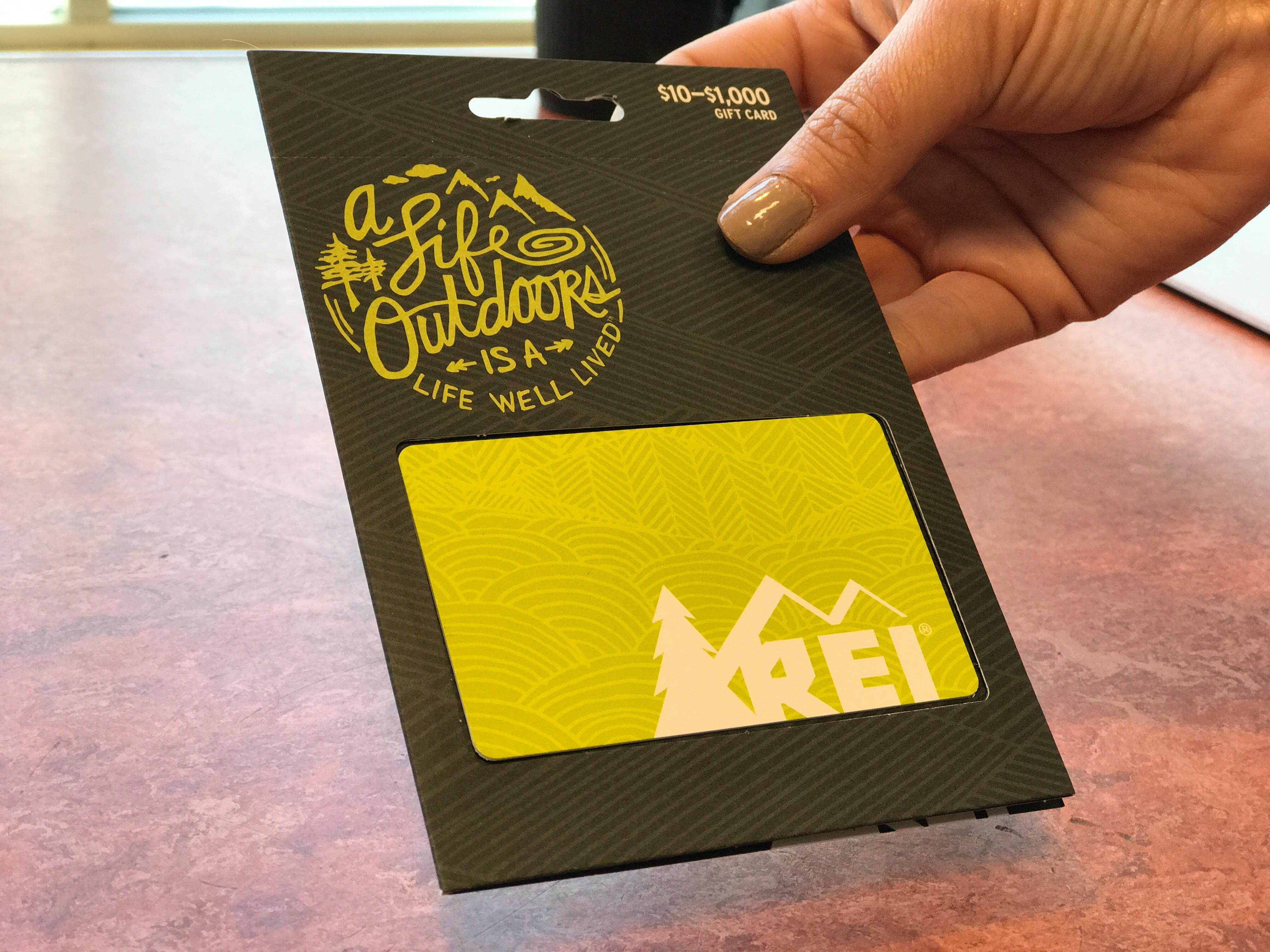 earn free gift cards - A person holding an REI gift card.