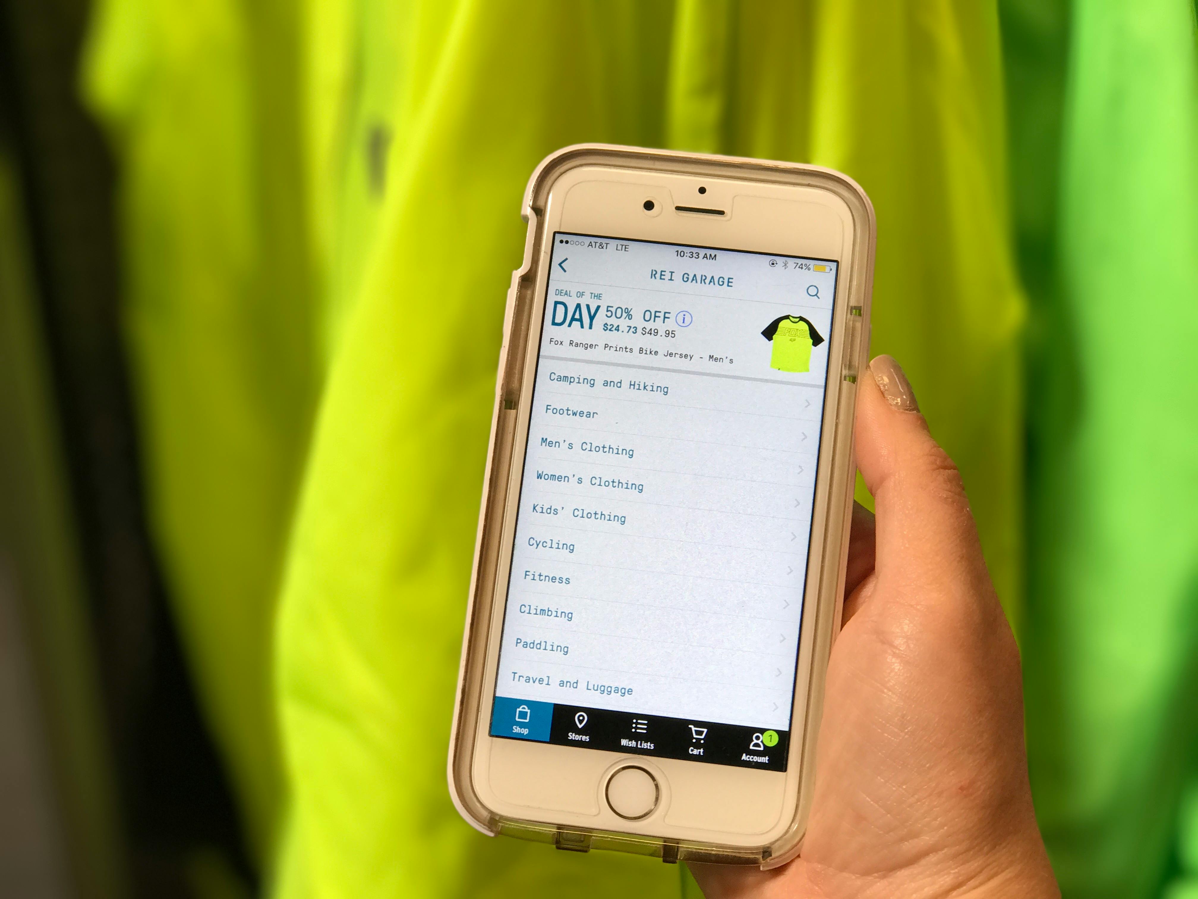 A person's hand holding up their phone with a page of REI's Deals of the Day displayed on the screen.