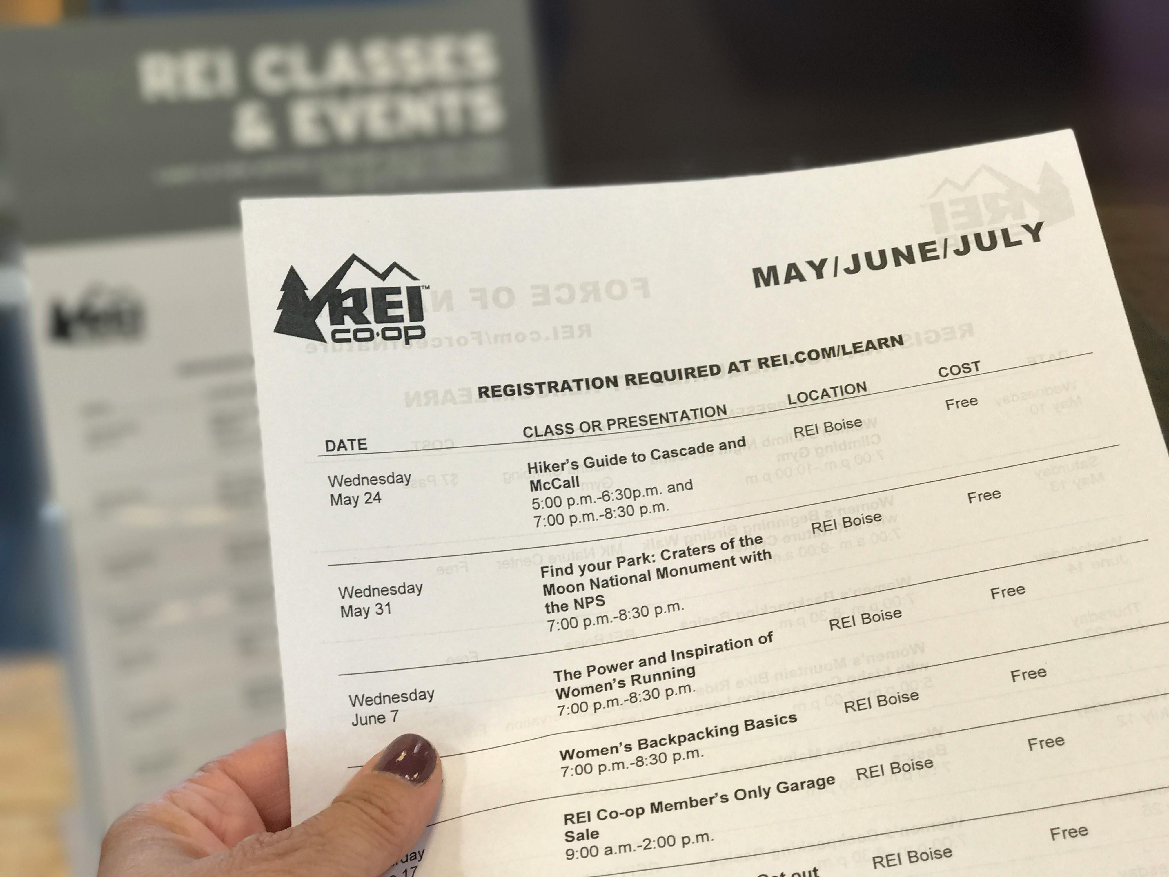 A person's hand holding a piece of paper with REI's schedule of classes and presentations for the months of May, June, and July.