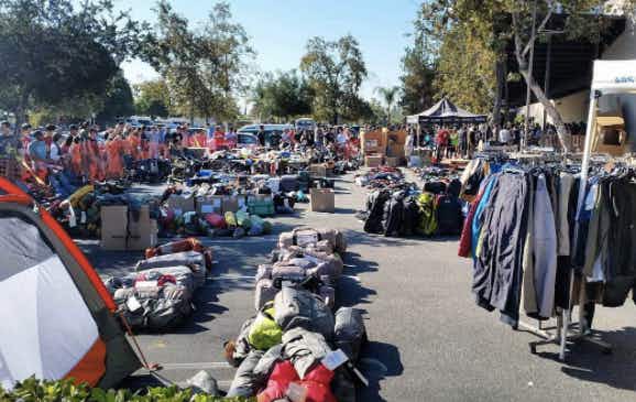 A sale set up in a parking lot with racks of clothes and camping equipment.
