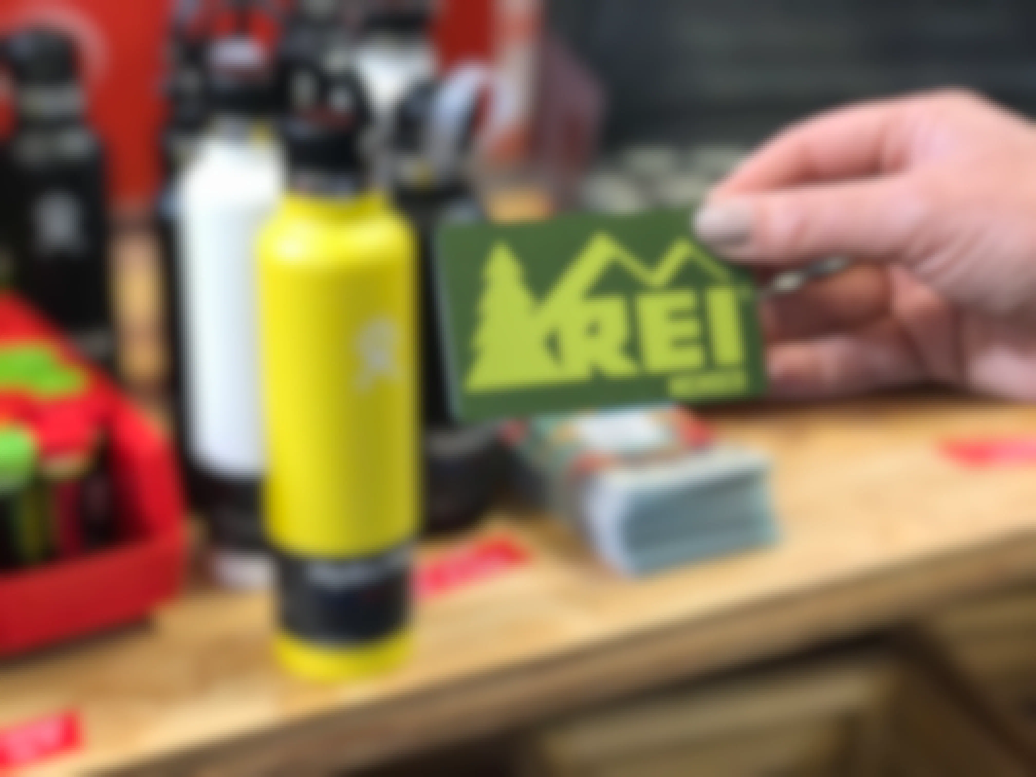 A person's hand holding a REI Member card in front of a shelf at REI.