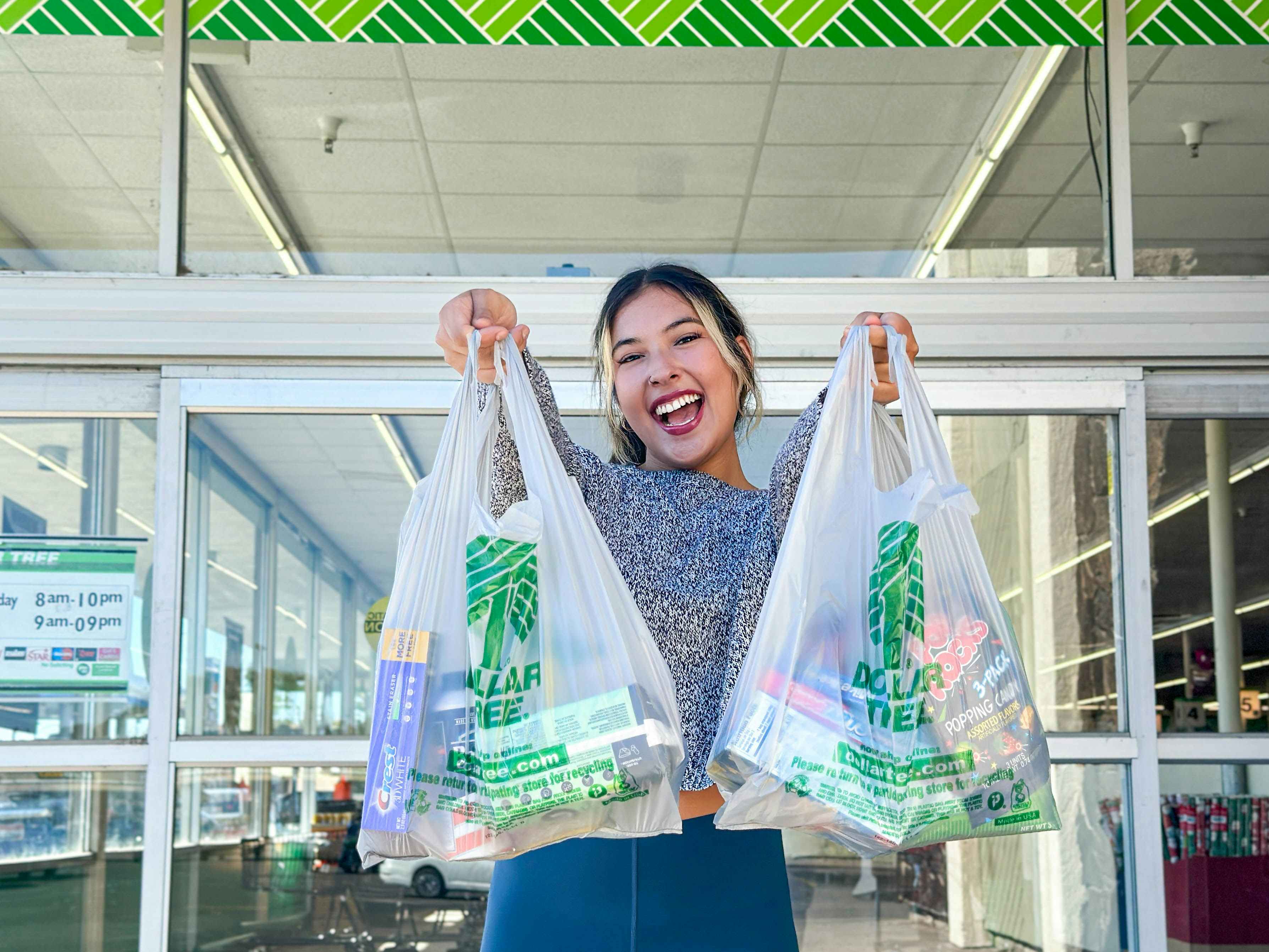 a woman holding up dollar tree bags outside store