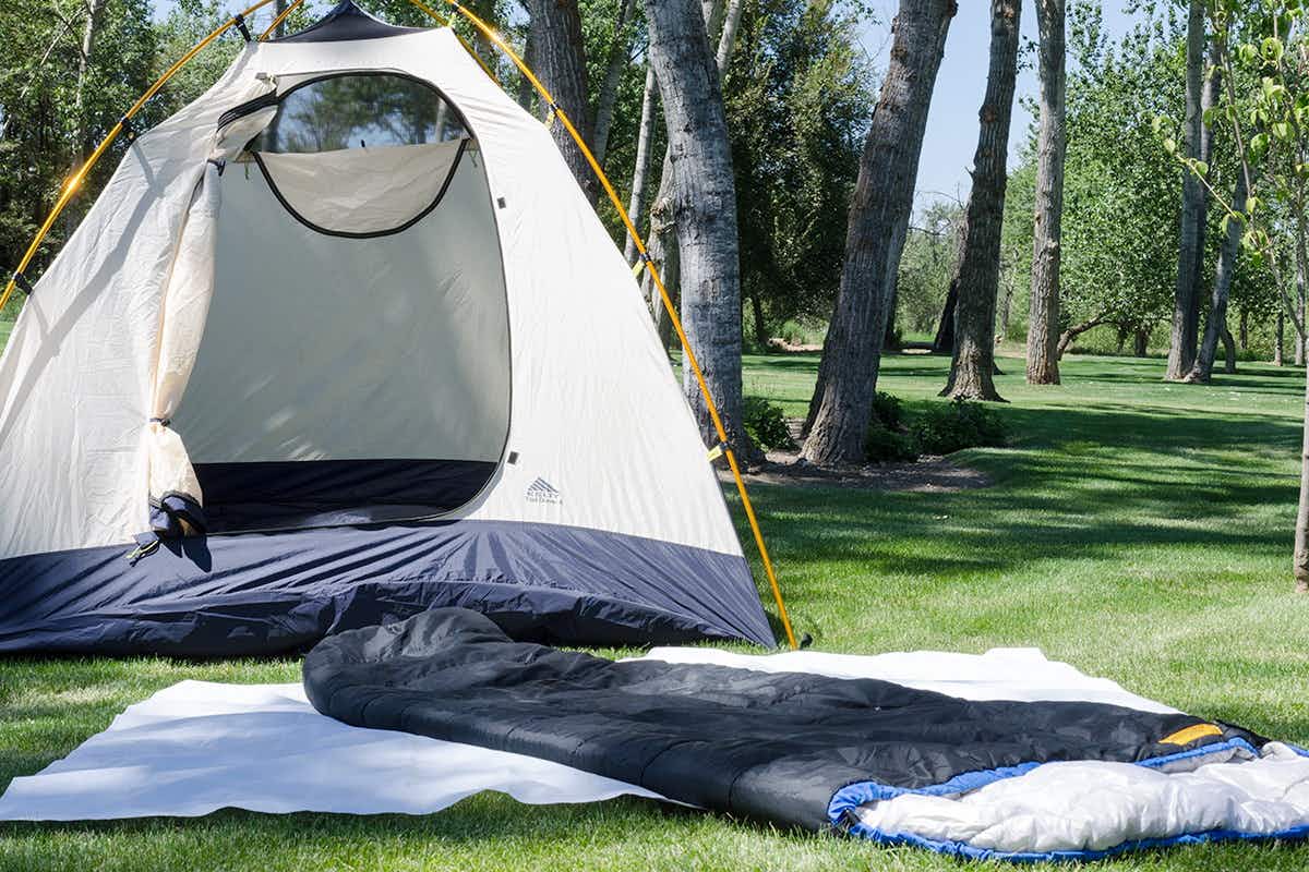 A tent set up in a backyard with a sleeping bag nearby.