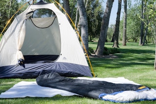 A tent and a sleeping bag set up on a lawn.