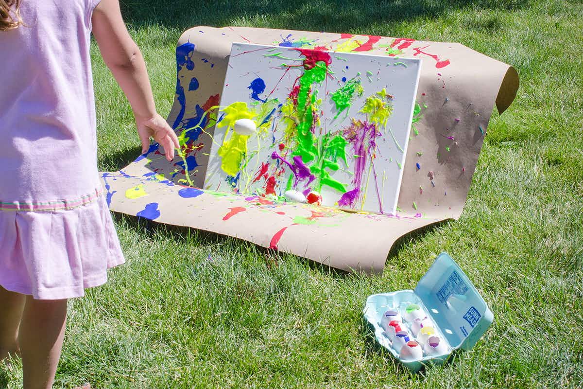 A girl throwing eggs full of paint at a canvas in a yard.