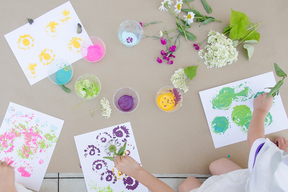 Kids using flowers as paint brushes to create art.
