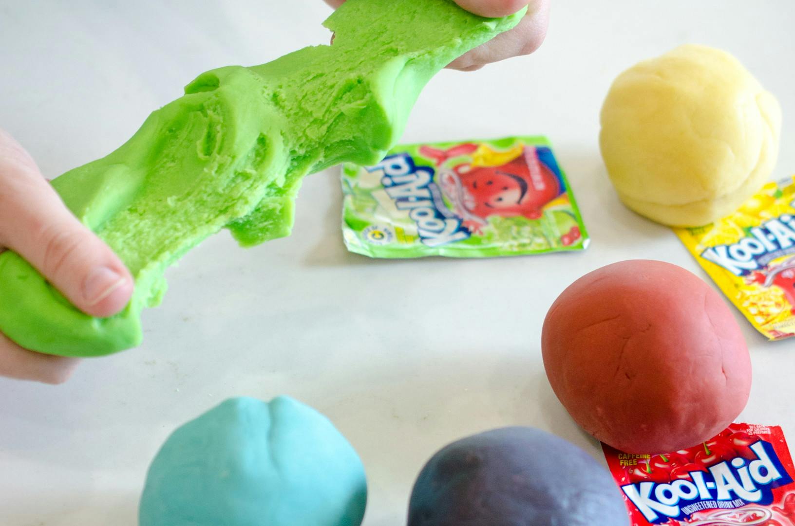 Green playdough being stretched out with packets of Kool-Aid nearby.