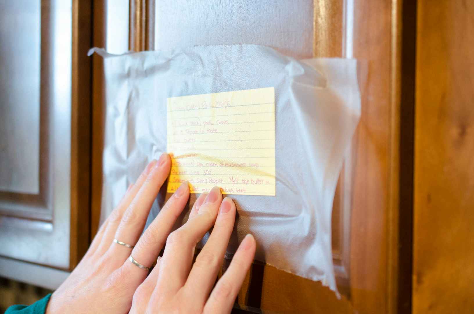 Someone sticking a recipe card to a cabinet with Press'n Seal to keep it clean and at eye level.