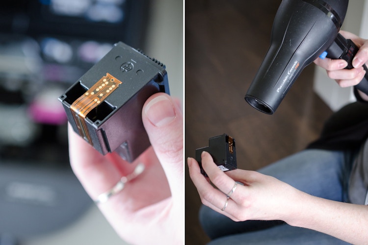 Someone using a blow dryer to heat up and thin ink in a printer cartridge.
