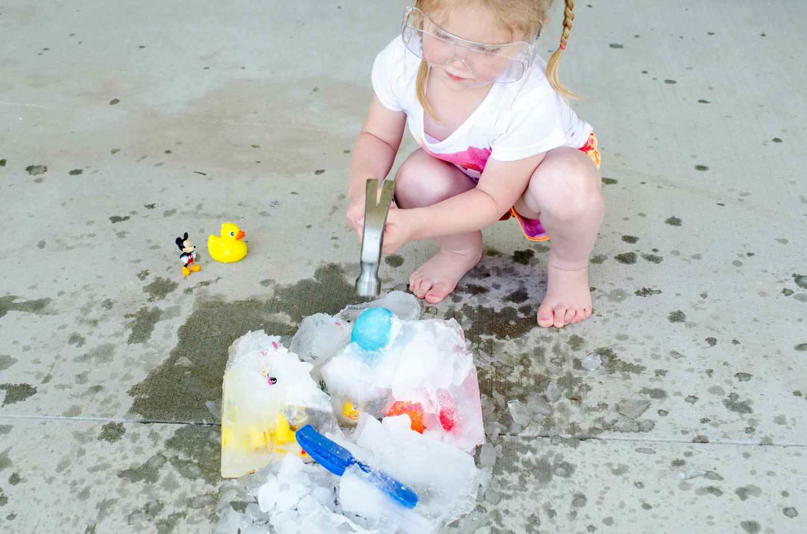 Little girl using a hammer to break apart ice with frozen toys inside.
