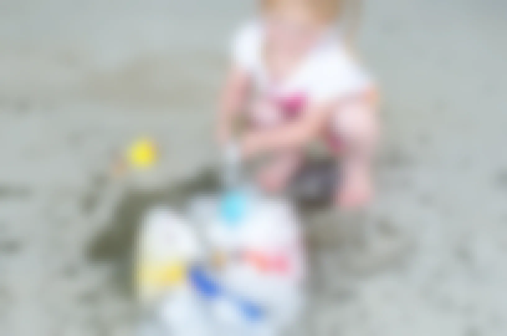 Little girl using a hammer to break apart ice with frozen toys inside.