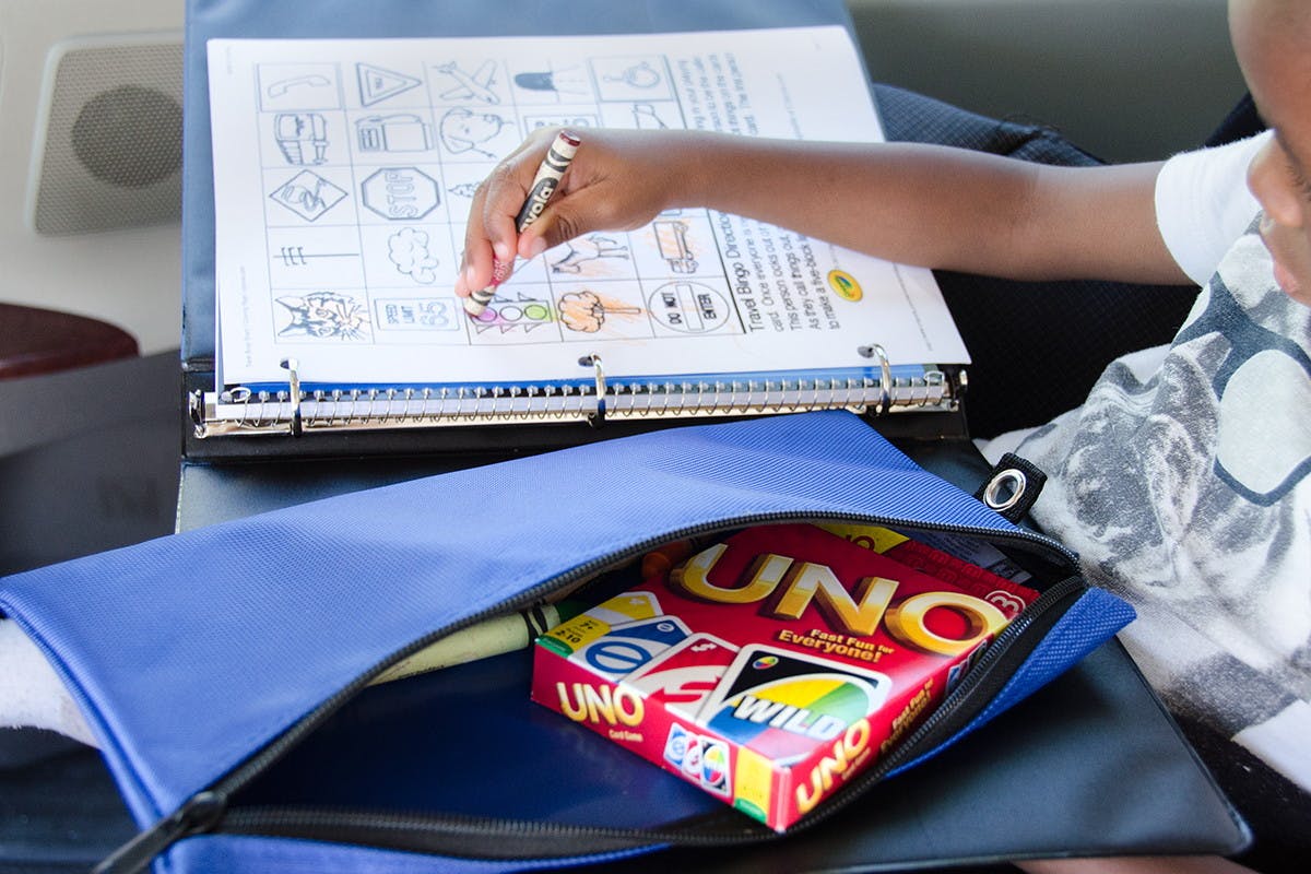 A boy coloring on a page placed in a binder with games in a pencil pouch nearby.
