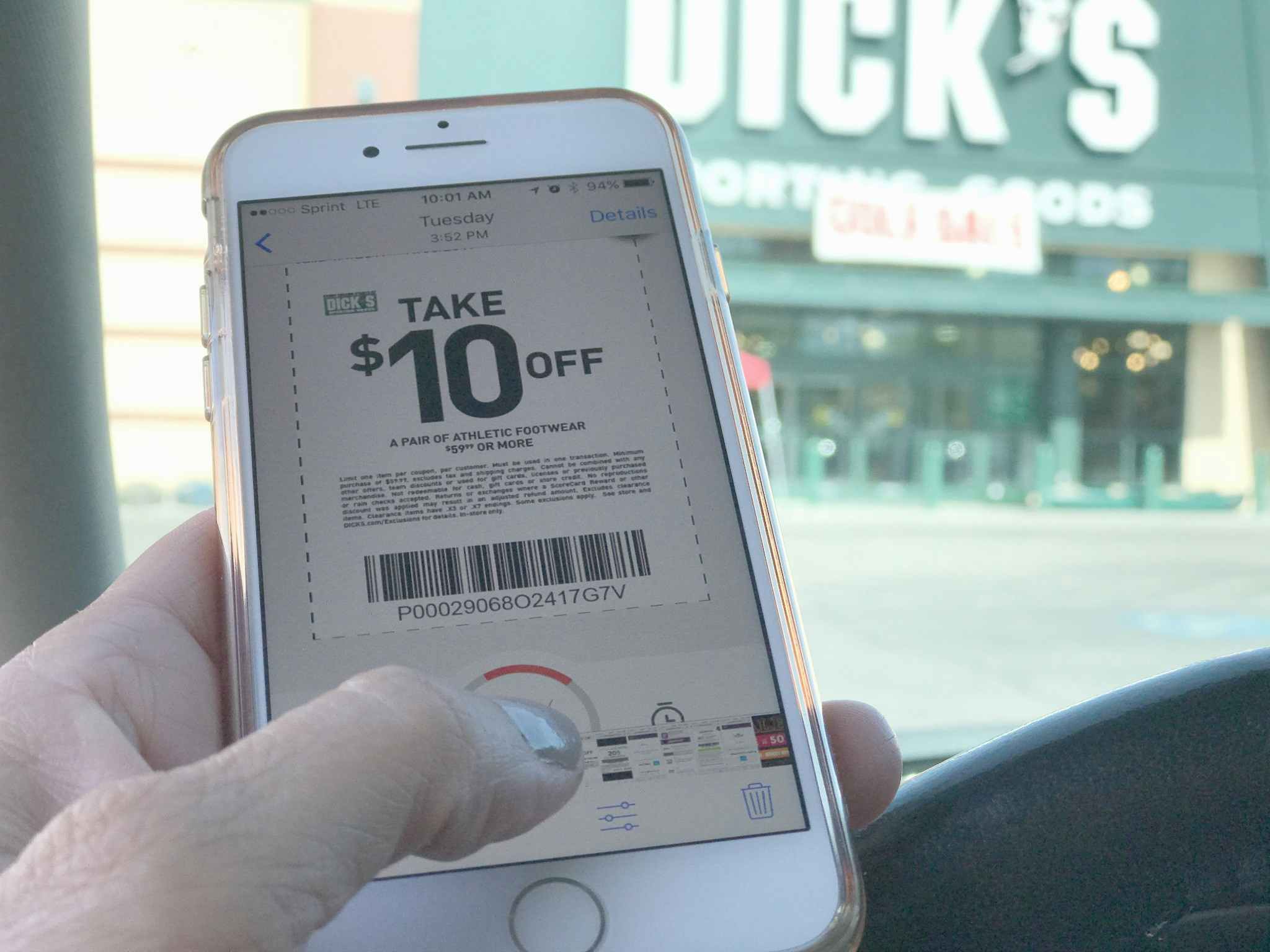 Someone holding a cell phone displaying a Dick's Sporting Goods coupon in front of a Dick's store front