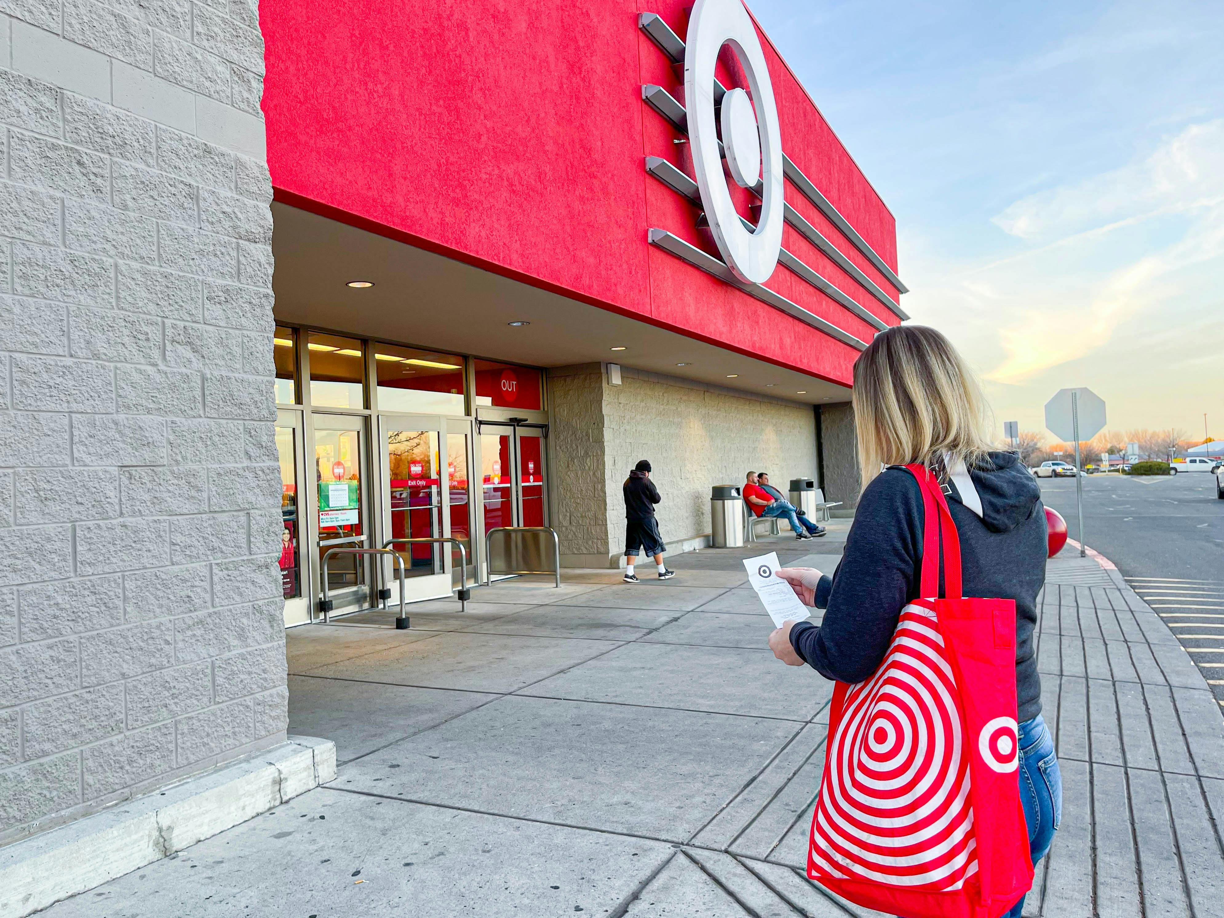 A person walking toward the Target entrance with a reusable Target shopping bag and holding a receipt.