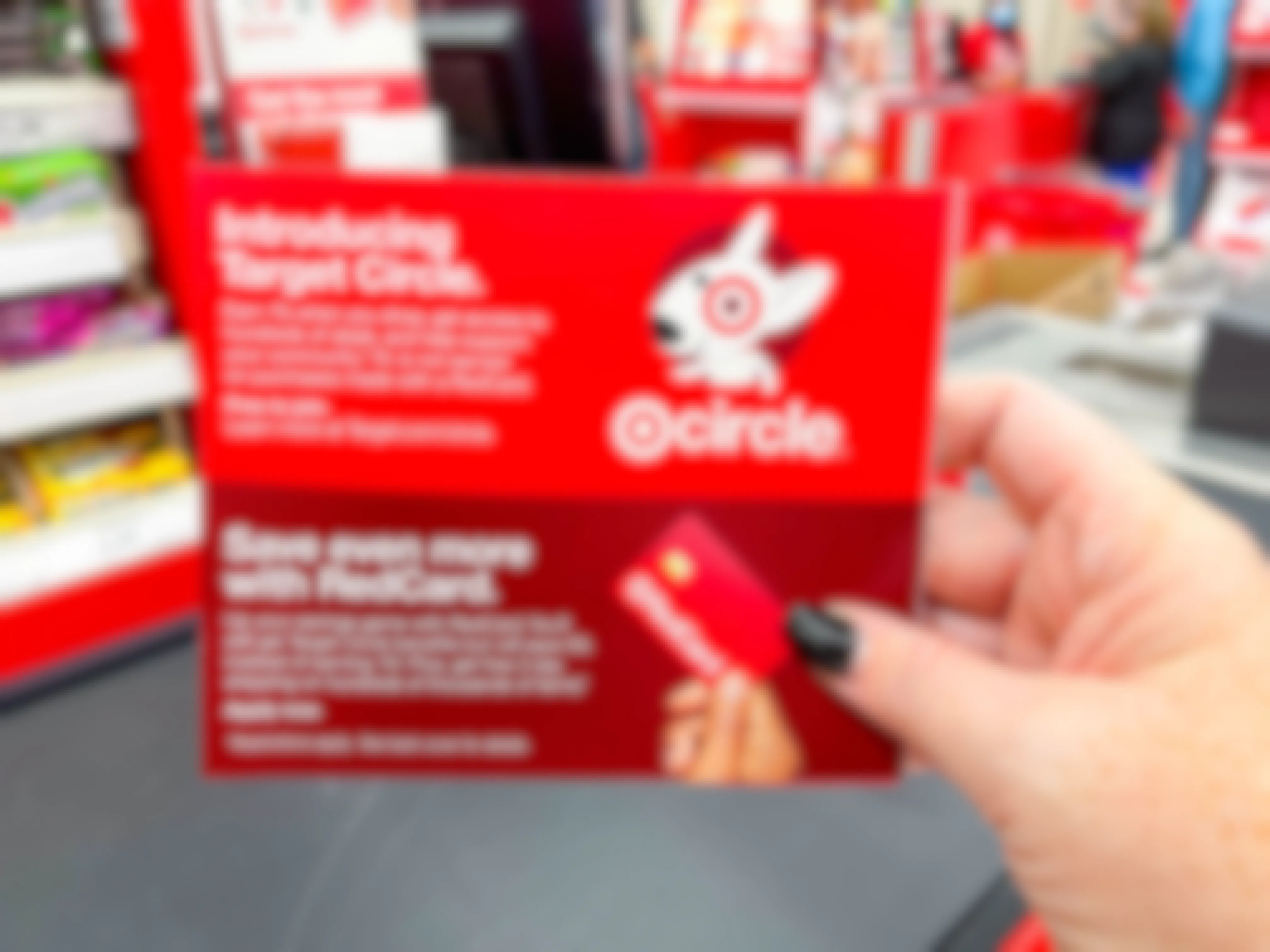 A person's hand holding a Target RedCard information card in front of the checkout lane at Target.