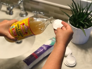 A woman applying apple cider vinegar to a cotton swab