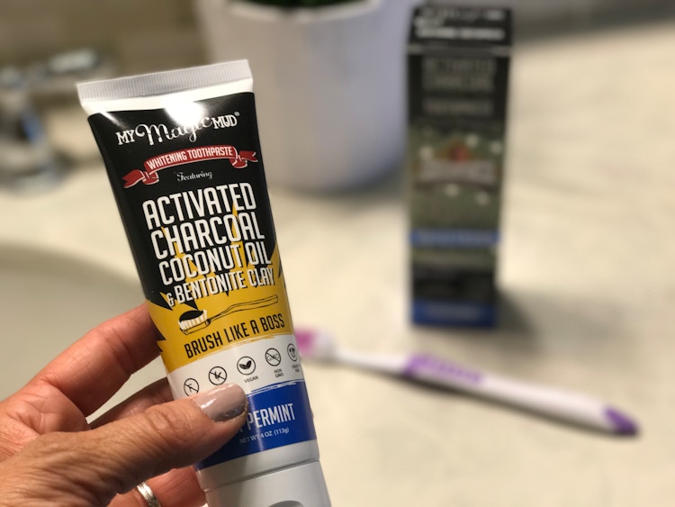 activated charcoal in a persons hand with a tooth brush out of focus in the background