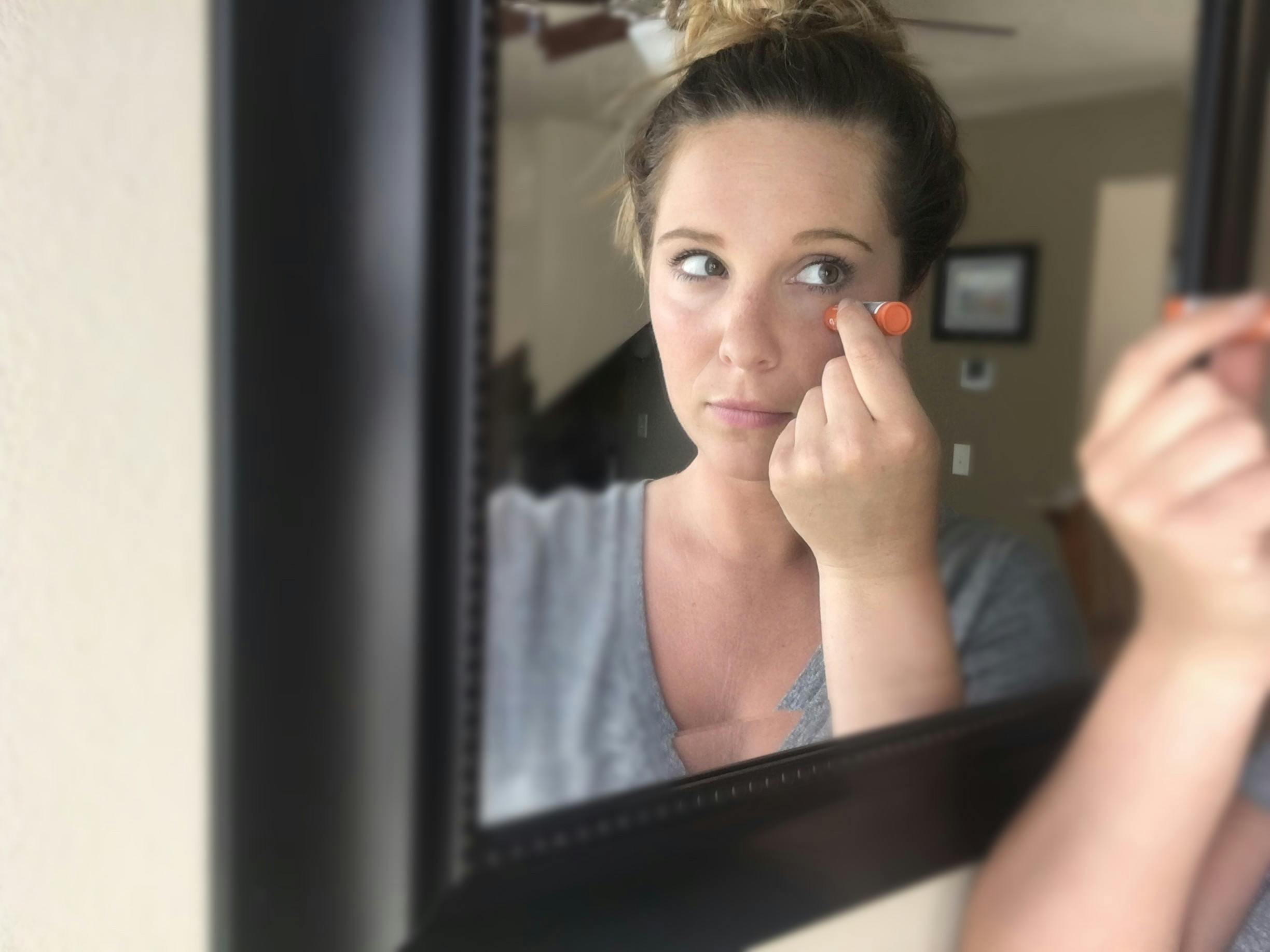 A woman reflected in the mirror, applying lip balm to the bags under her eyes