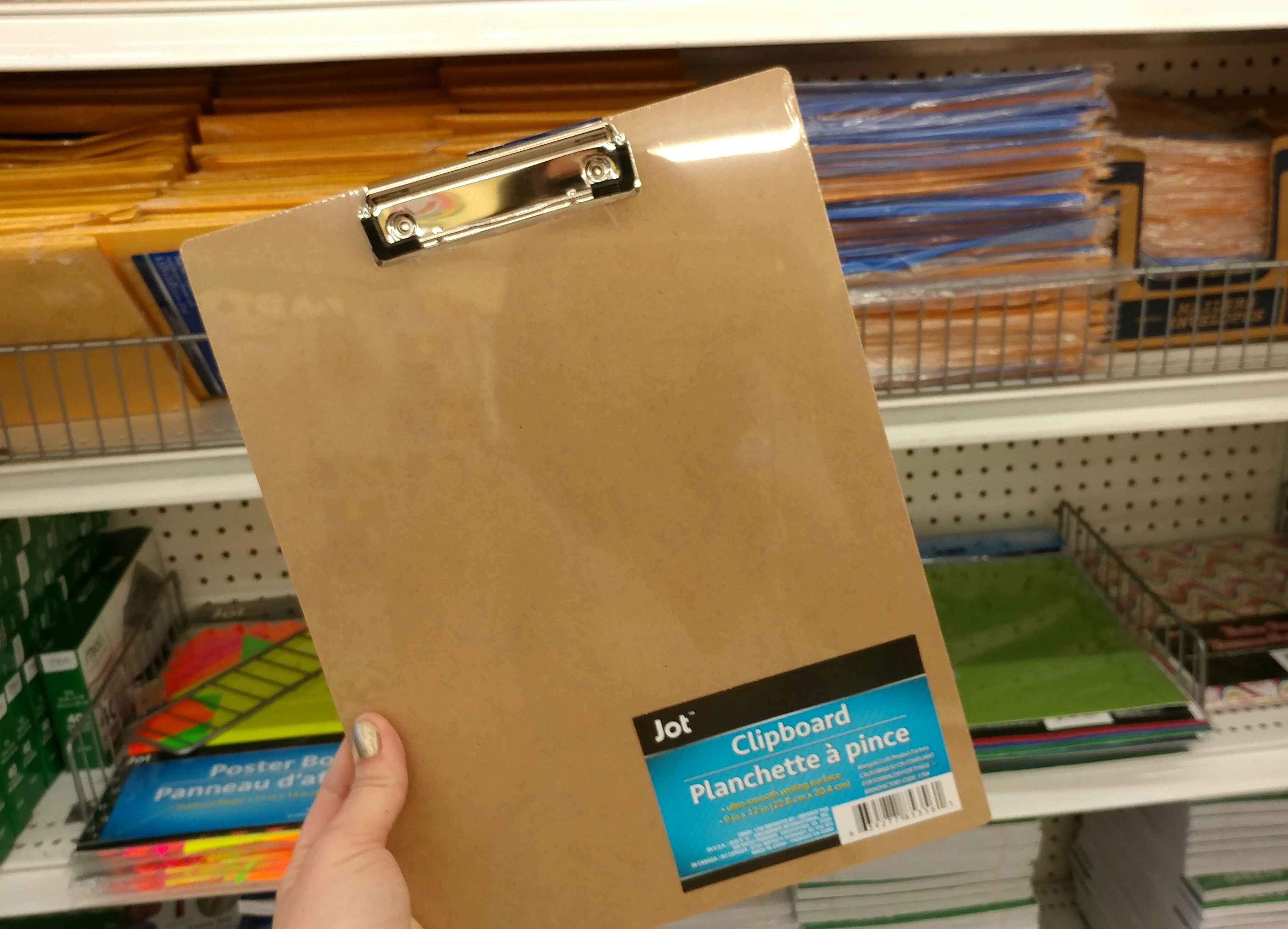 A person's hand holding an empty clipboard in front of a shelf at Dollar Tree.