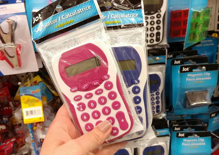 A person's hand holding up two calculators in front of a display of calculators for sale at Dollar Tree.