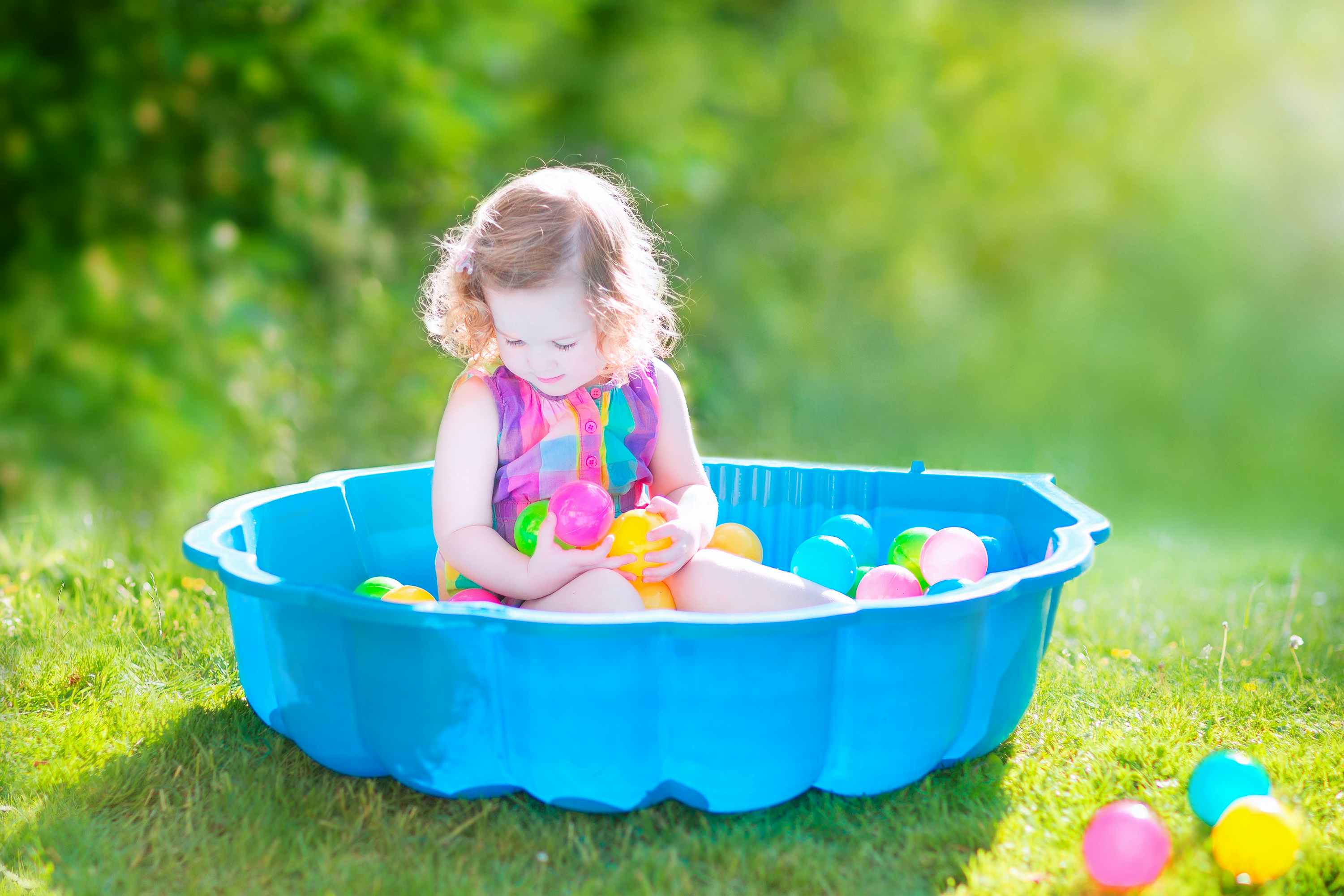 A little girl playing outside in a kiddie pool filled with ball pit balls