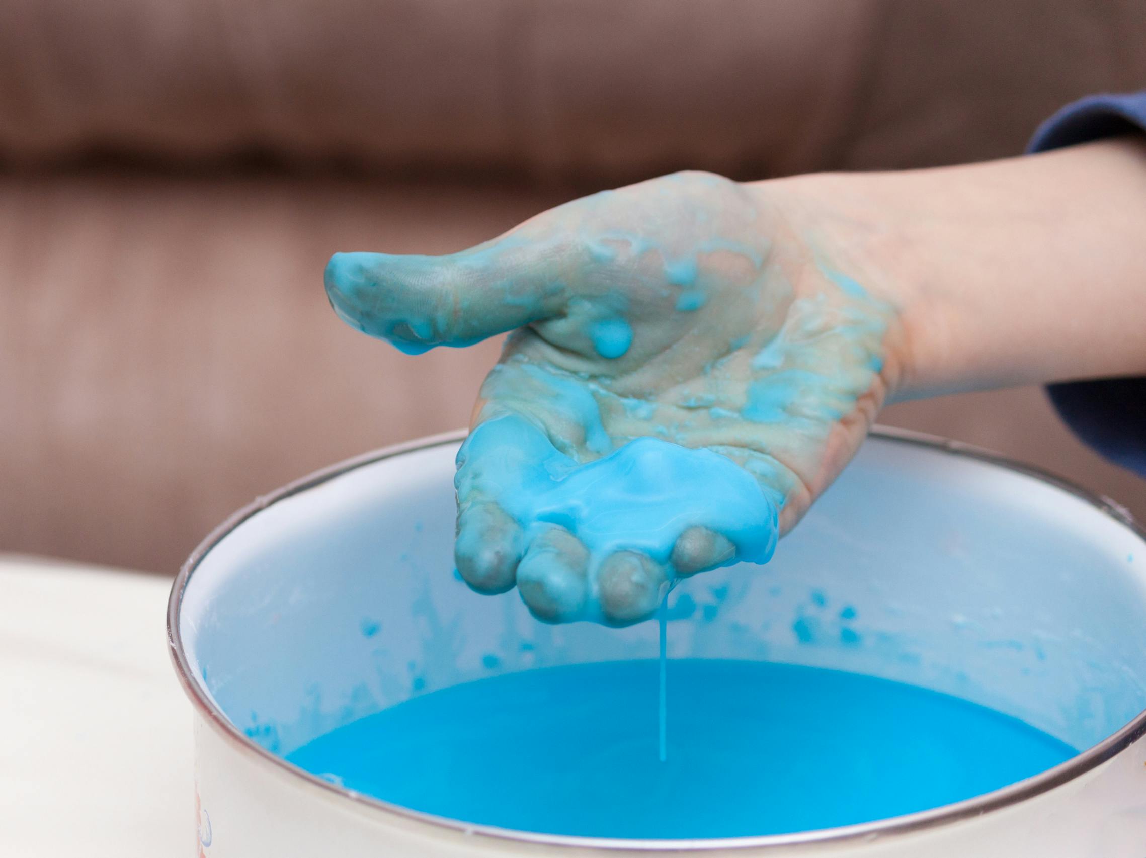 A childs hand holding some cornstarch and water mixture that has been dyed blue over a bowl of the mixture