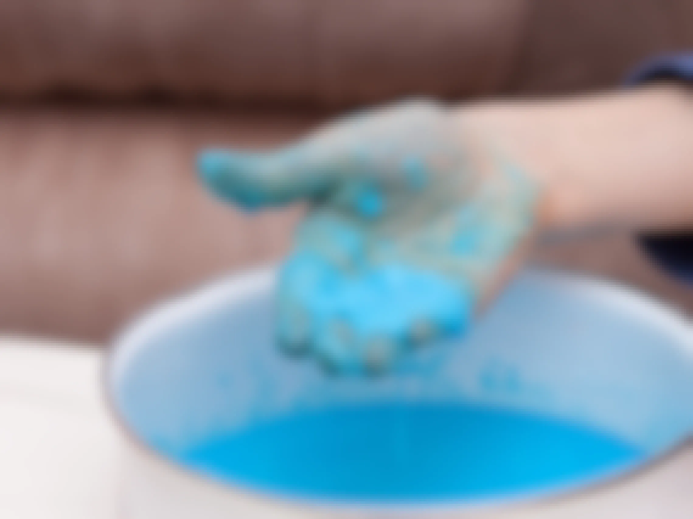 A childs hand holding some cornstarch and water mixture that has been dyed blue over a bowl of the mixture