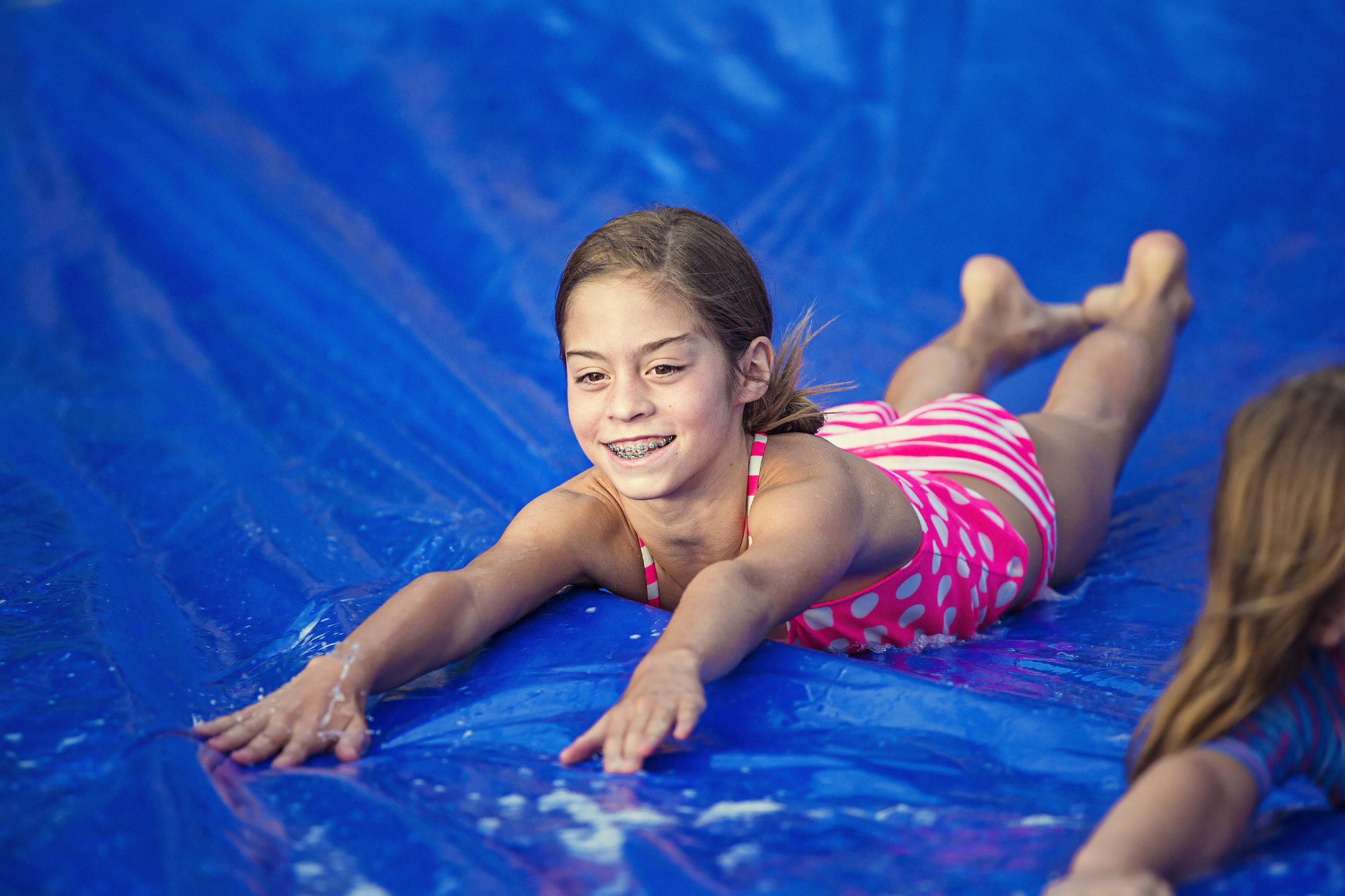 A girl in a bathing suit sliding down a blue tarp being used as a slip n slide