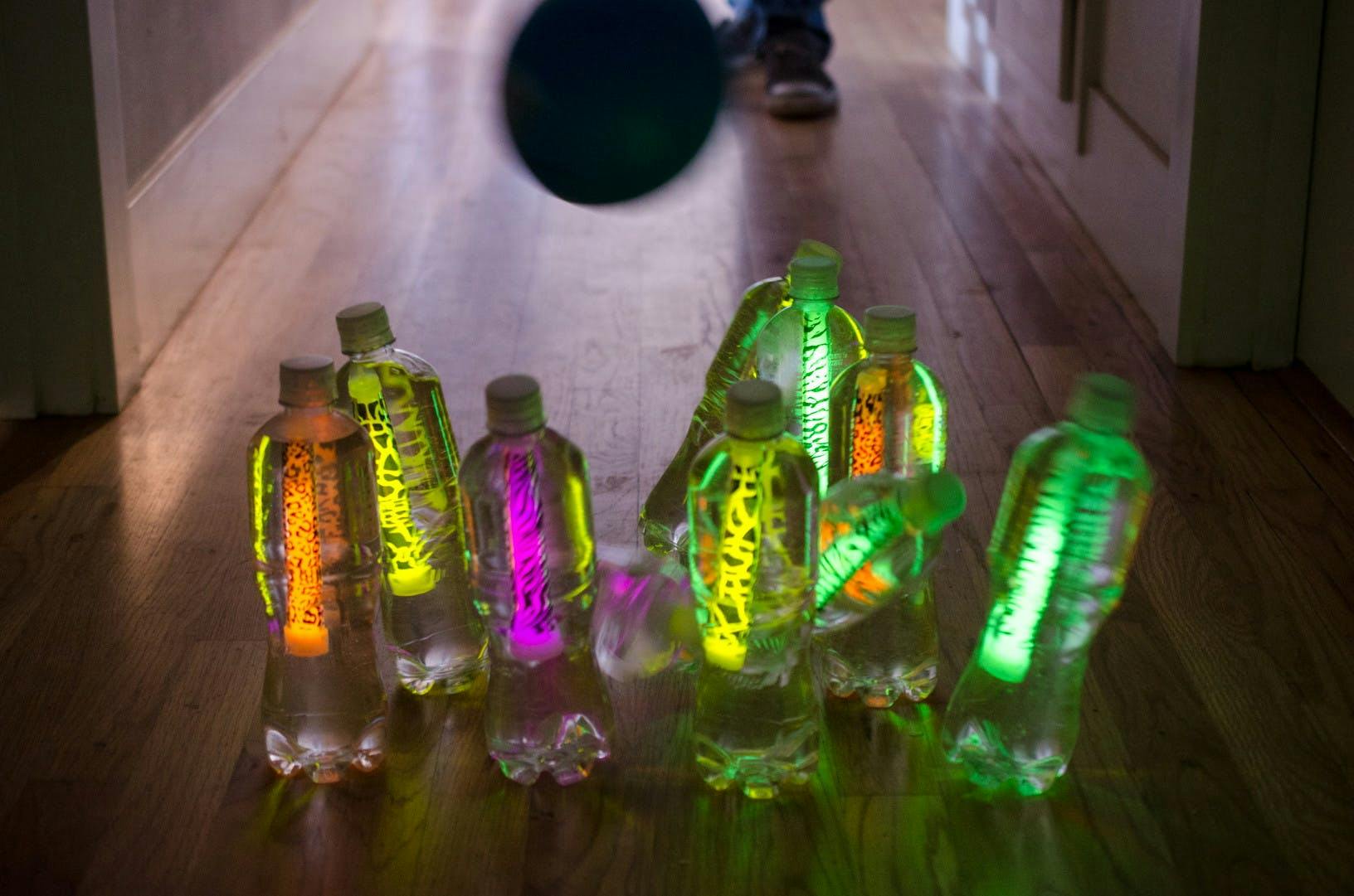 Water bottles with glow sticks in them illuminating a dark hallway in the form of bowling pins, and a ball rolling at them