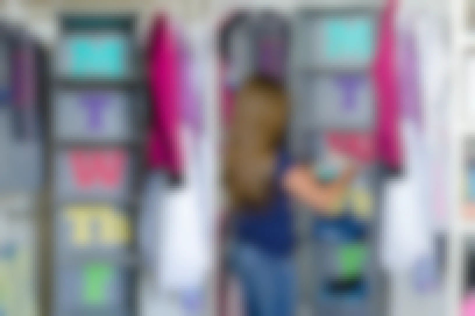 A girl placing clothes in a hanging closet organizer with the cubbies labeled for each day of the week.