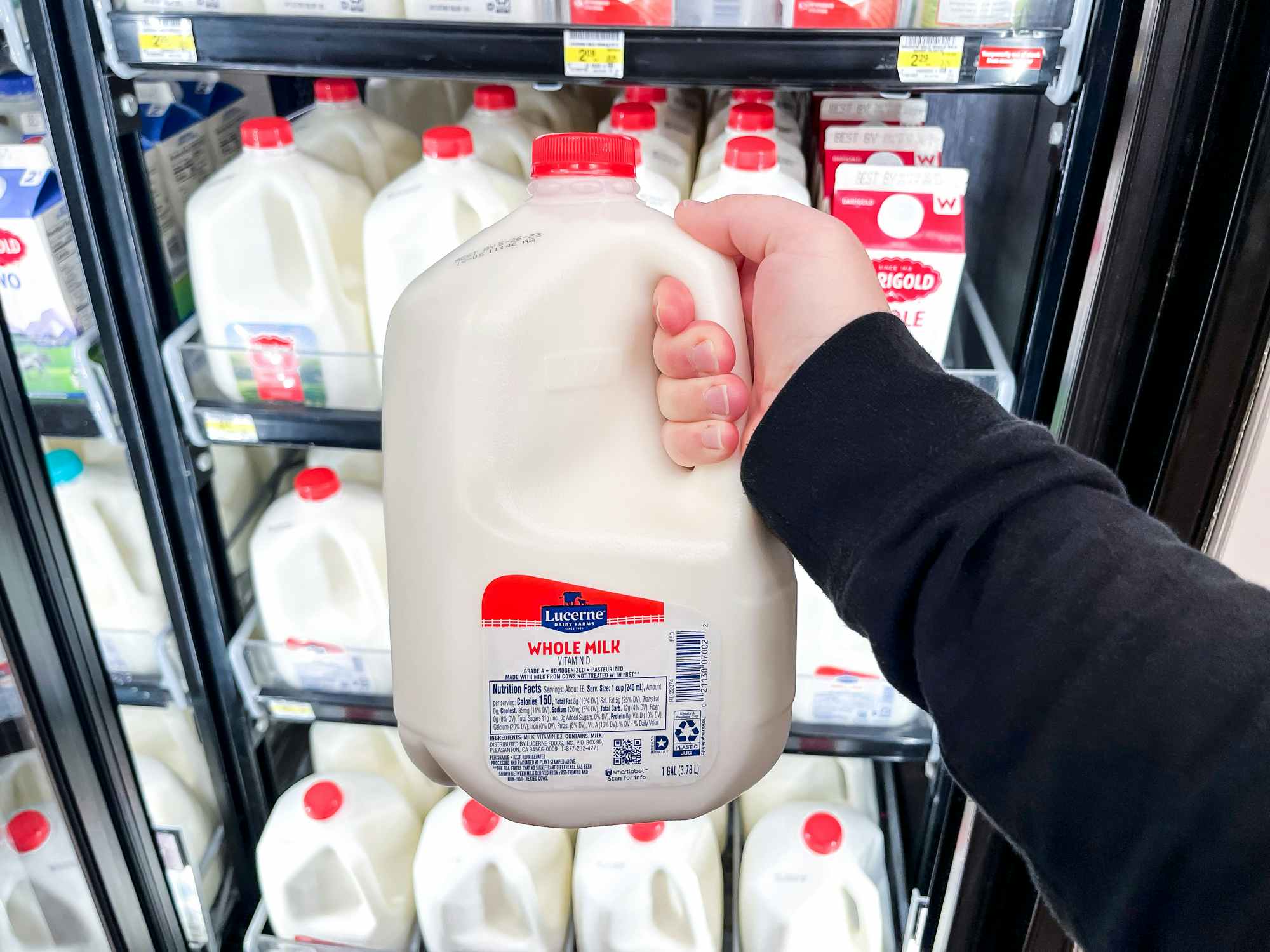 Someone taking a gallon of milk out of a refrigerated shelf in a store