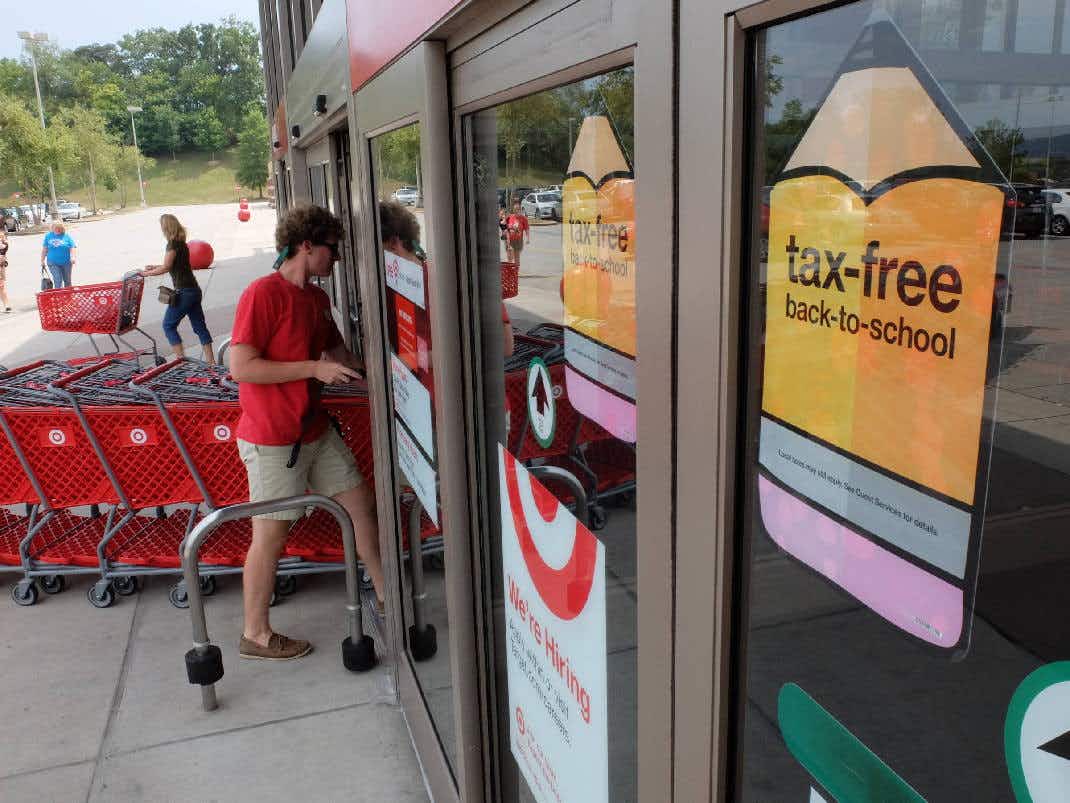 A Target employee walking into a Target store that has signs in the window announcing the tax-free back-to-school shopping weekend.
