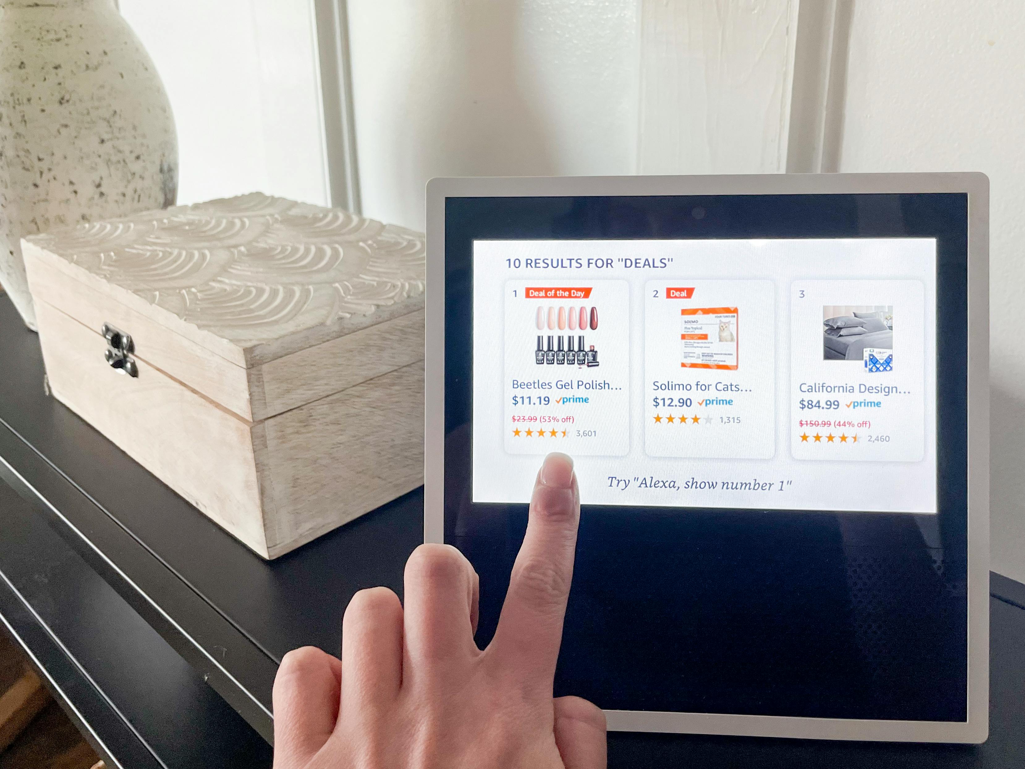 a woman's hand pointing to an amazon prime day deal featured on their echo show