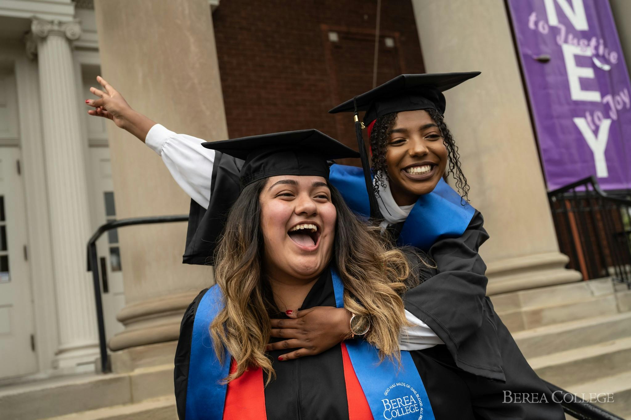 Two smiling students wearing graduation caps and gowns on some steps at Berea College.