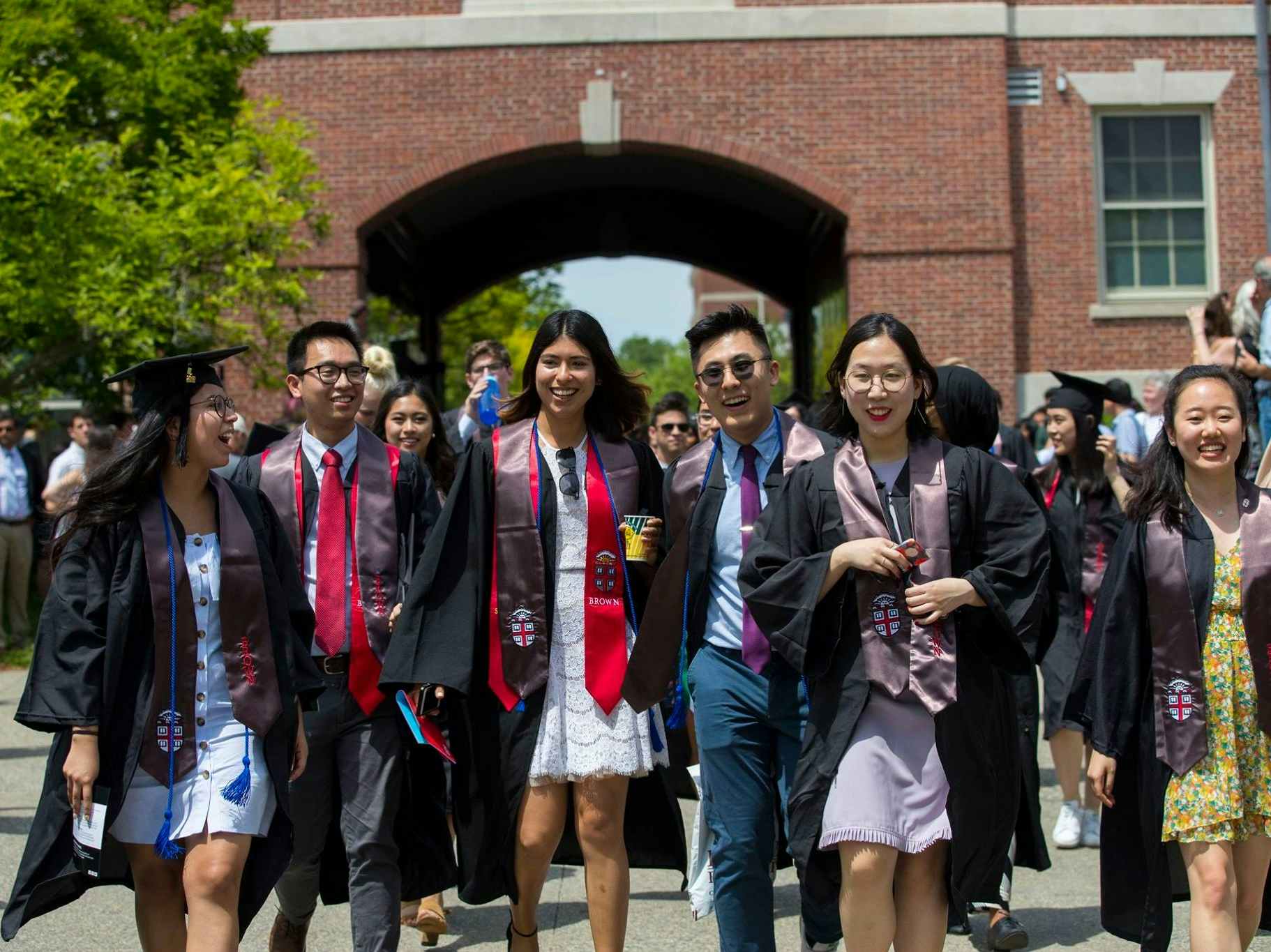 A group of students walking at Brown University wearing graduation gowns.